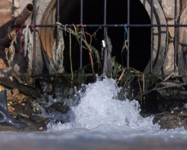 Sewer jetting services in action as high-pressure water blasts through a clogged underground pipe grate.