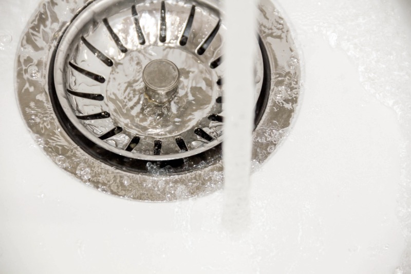 A close-up of a perfectly draining white kitchen sink basin, showcasing a clear pipe after expert drain cleaning services.
