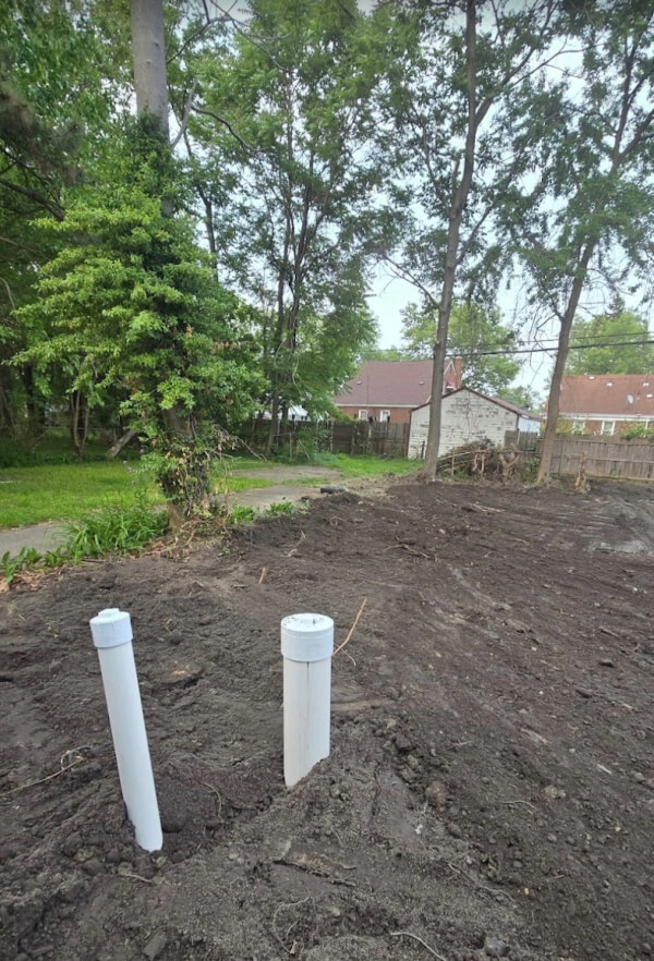 A residential yard with exposed, graded dirt and new PVC access pipes installed during professional underground plumbing repair services.